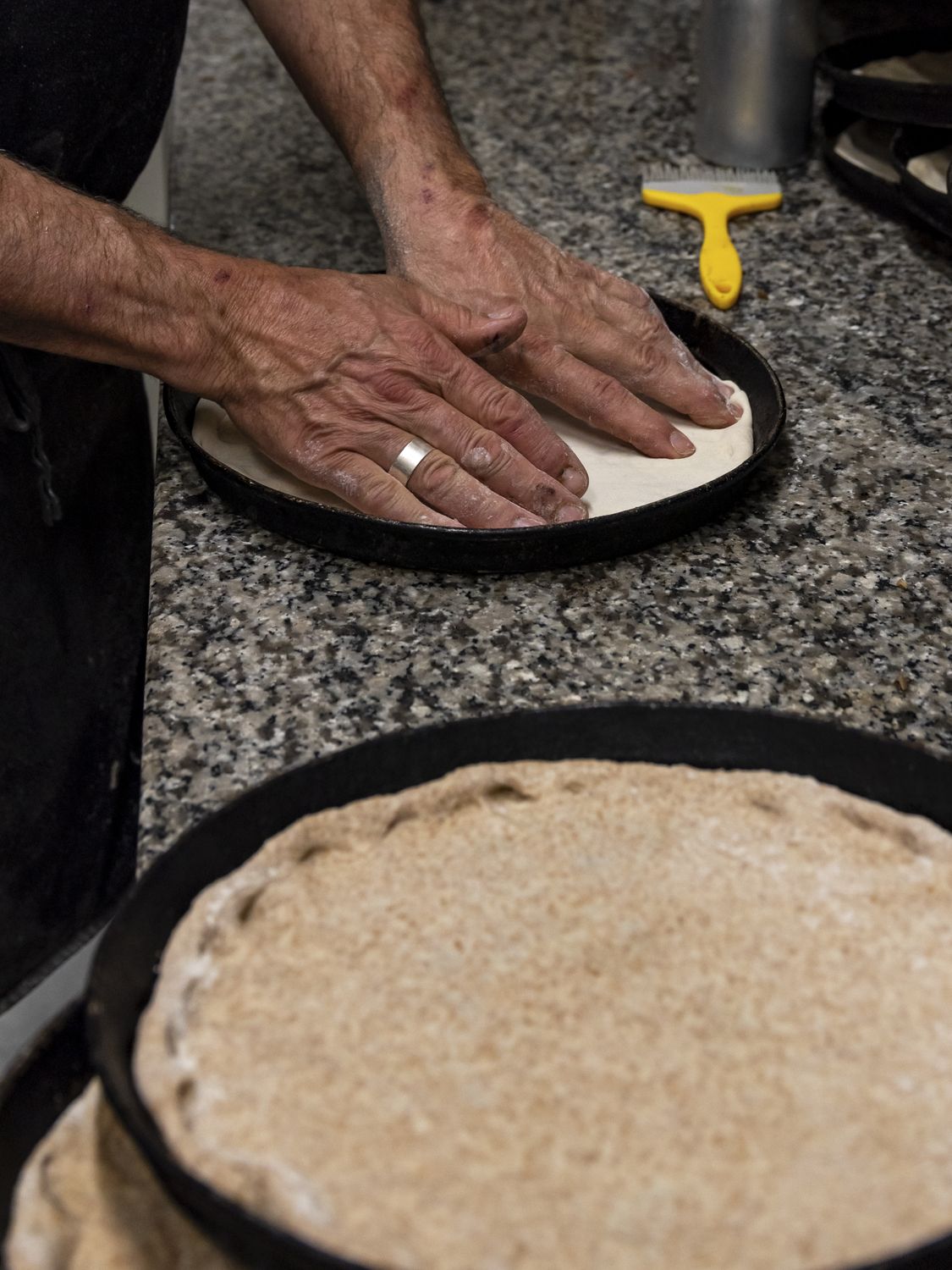 Le mani del pizzaiolo stendono l'impasto in teglia